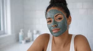 Mixed race woman with clay mask applied, seated at a bright bathroom counter, unbothered expression, skin detox myth editorial.