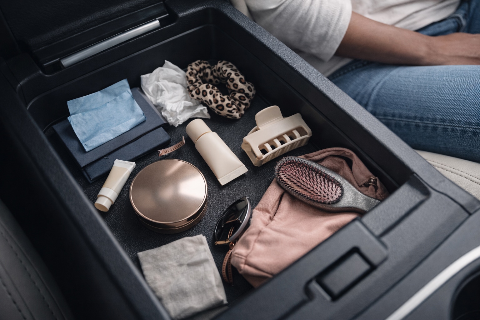 Doing makeup in the car essentials in a busy center console with lip balm, compact, mini SPF, hair clip, and a coffee cup at a red light.