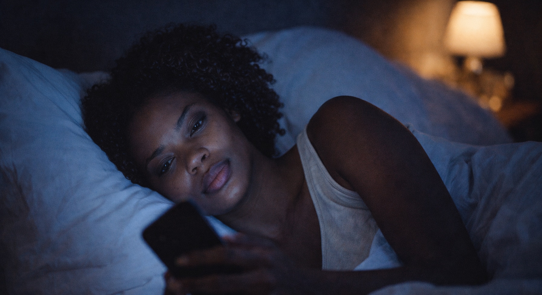 Black woman scrolling phone late at night in bed — the quiet drain of social comparison on confidence and beauty